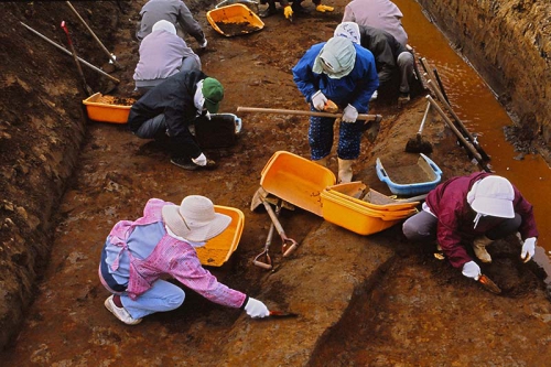 発掘作業員がスコップなどの道具を使って遺構の中に埋まった土を掘っている様子